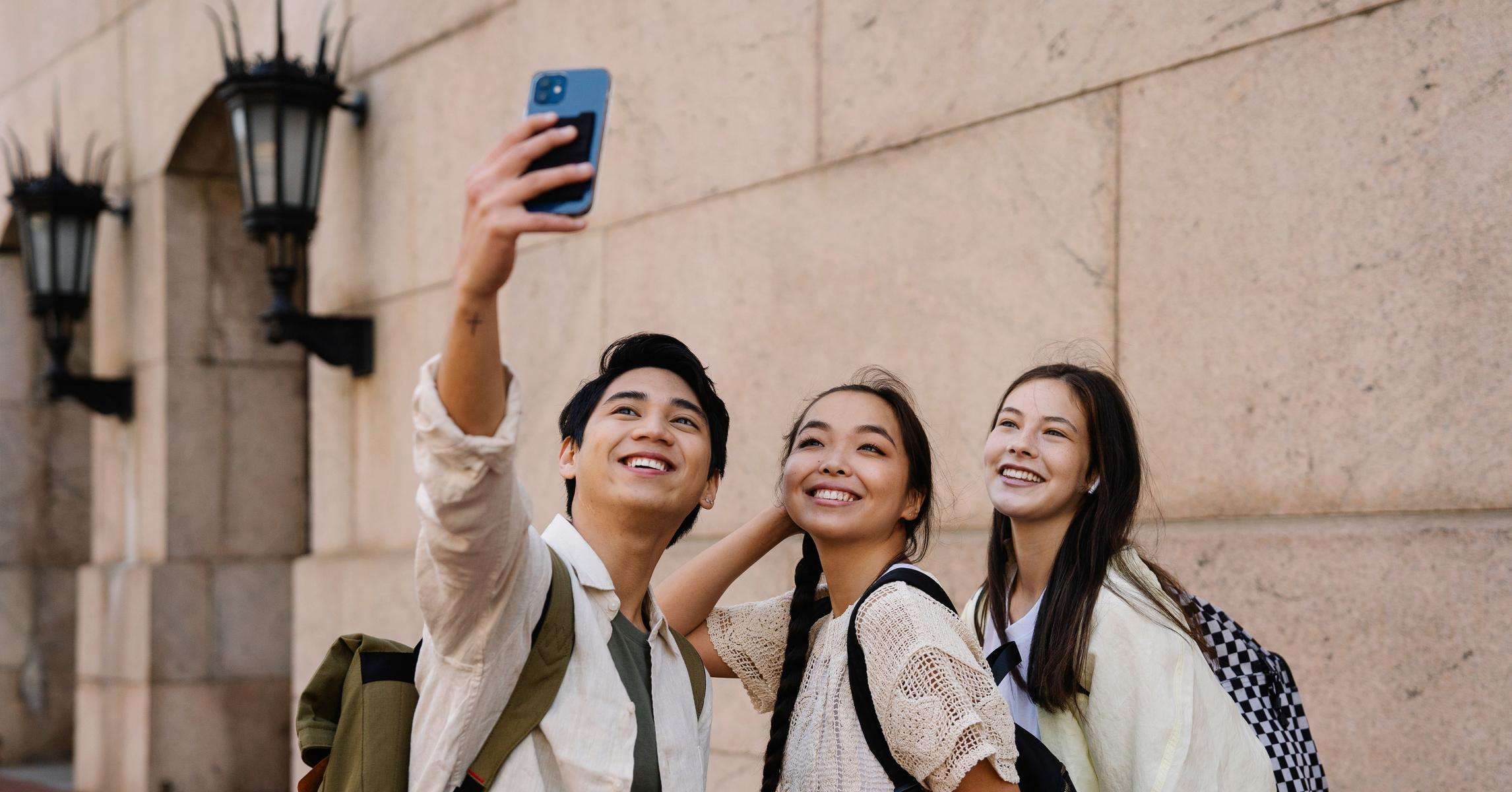 Ba người bạn cùng chụp ảnh selfie ngoài trời trong một chuyến đi, đeo balo du lịch