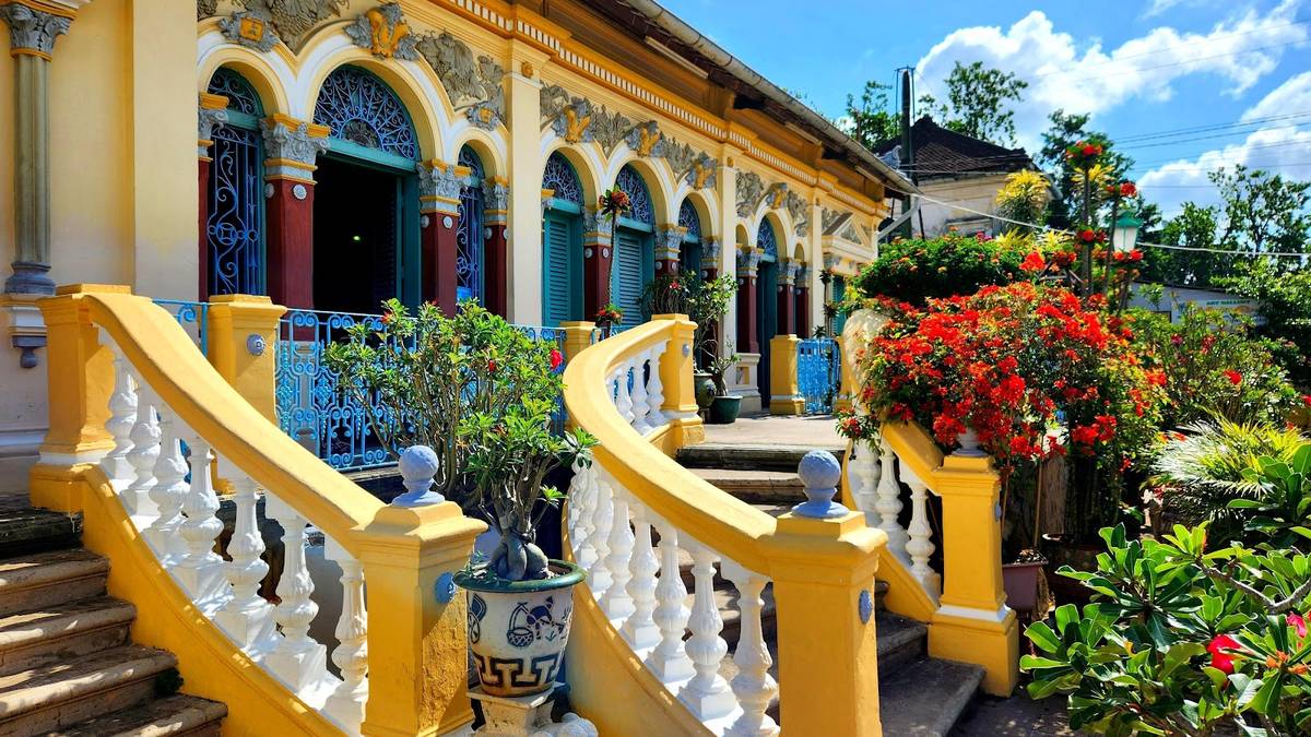 Mặt tiền vàng và cầu thang đôi của nhà cổ Bình Thủy Cần Thơ, hoa giấy đỏ, trời xanh