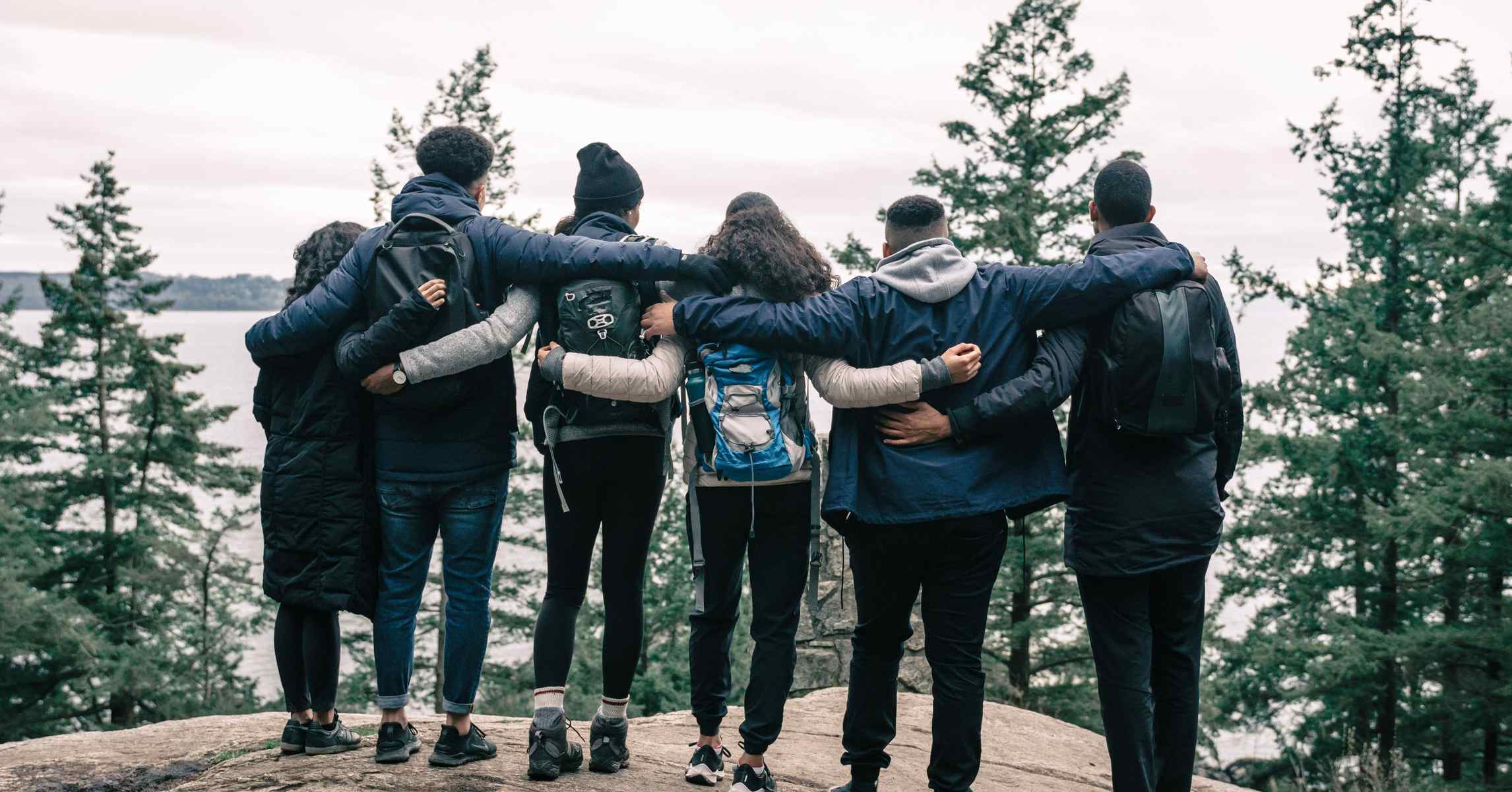 Nhóm bạn trẻ ôm vai nhau đứng trên vách đá ngắm thiên nhiên trong chuyến đi